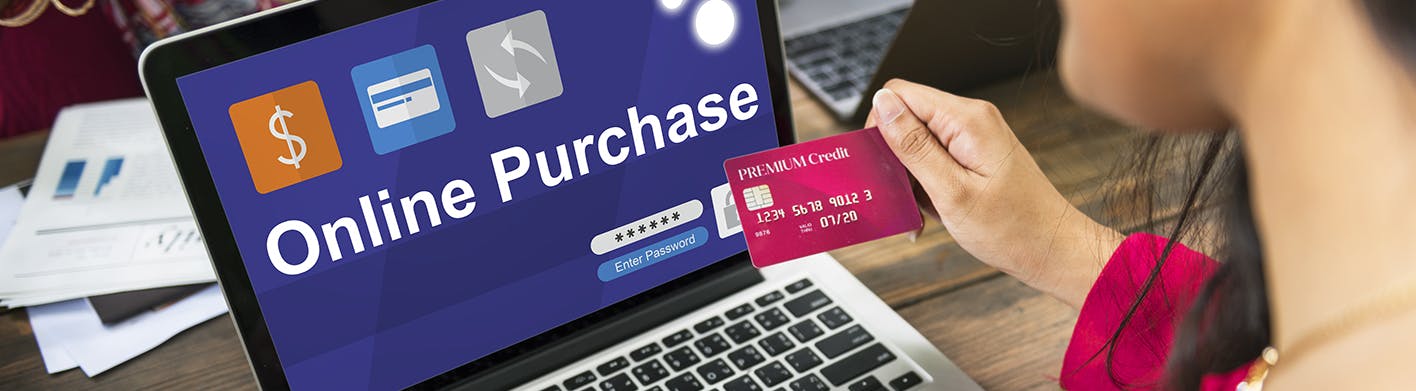 A hand holding a credit card making an online purchase on a website loaded on the screen of laptop